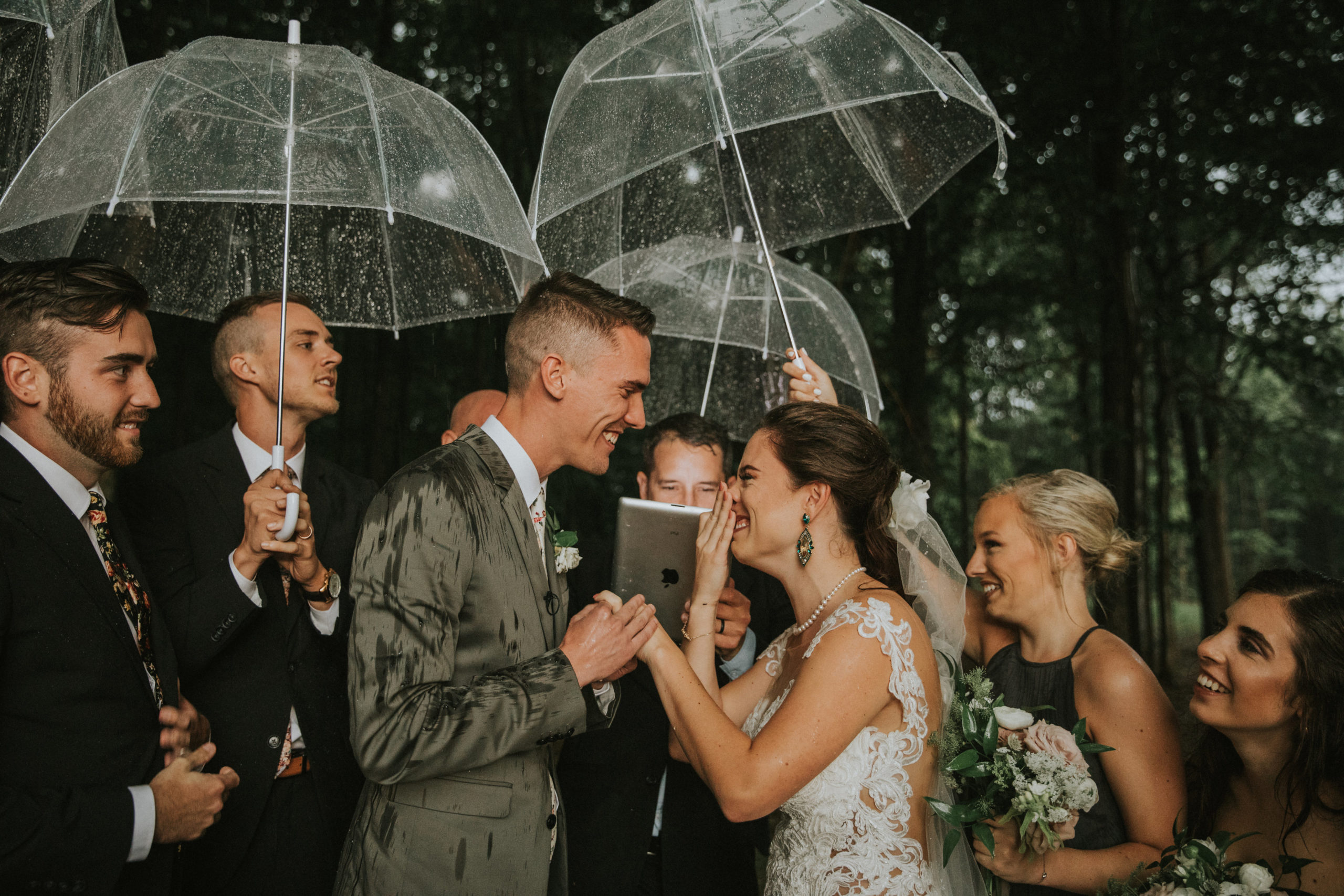 Bride and Groom standing under umbrellas getting married in the rain